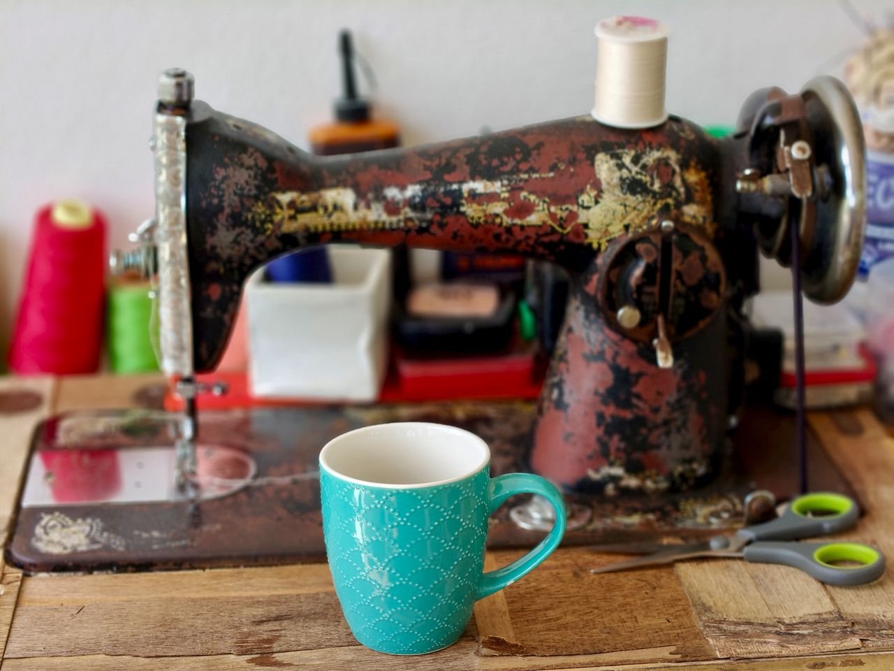 Rustic scene featuring an antique sewing machine with a teal mug placed on a wooden table.